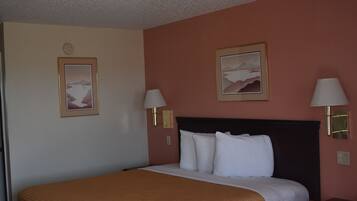 A hotel room with a large bed, two bedside lamps, a nightstand, and two framed pictures on the wall.