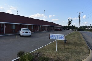 Un motel con fachada de ladrillo rojo, un estacionamiento y un letrero que indica la entrada.