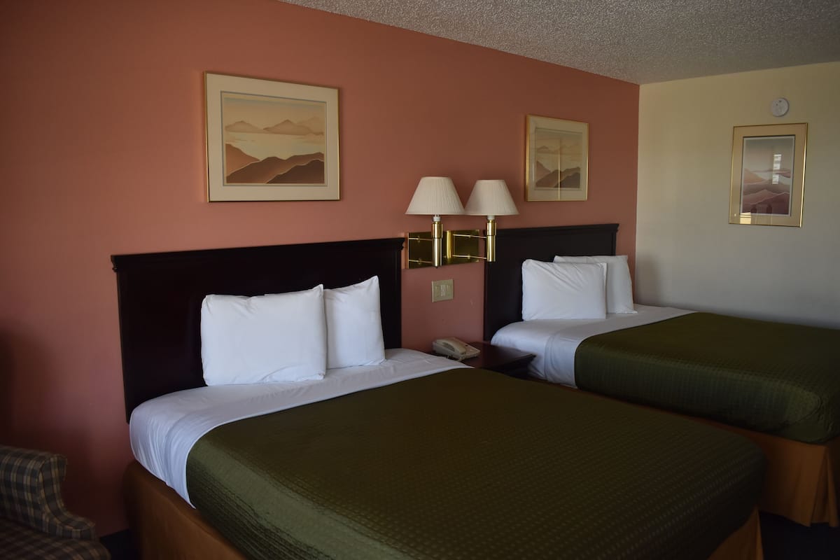 A hotel room with two beds, a nightstand with a lamp, and framed artwork on the walls.