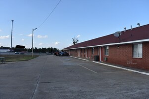 Un motel con fachada de ladrillo rojo, una antena parabólica y un estacionamiento con varios autos.