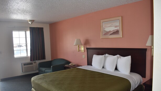 A hotel room with a large bed, a desk, a chair, and a window with curtains. - Royal Inn (Springdale)