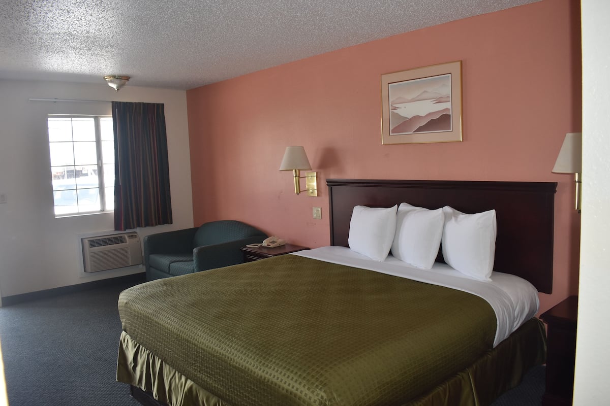 A hotel room with a large bed, a desk, a chair, and a window with curtains.