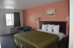 A hotel room with a large bed, a desk, a chair, and a window with curtains. - Royal Inn (Springdale)