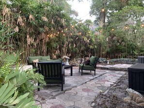 Un patio al aire libre con suelo de piedra, asientos acolchados verdes y luces colgantes.