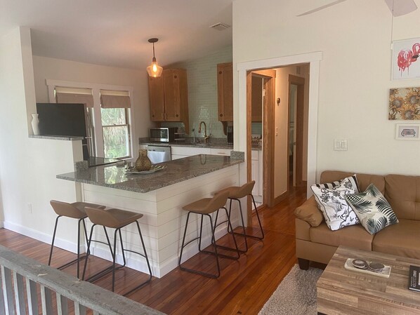 Una cocina moderna con una isla central, taburetes de bar y un comedor con sofá y cojines.