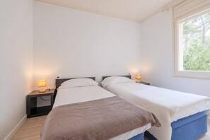 A room with two single beds, a window with a view of trees, and bedside lamps.