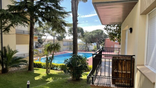 A residential building with a balcony overlooking a swimming pool, surrounded by trees and greenery.