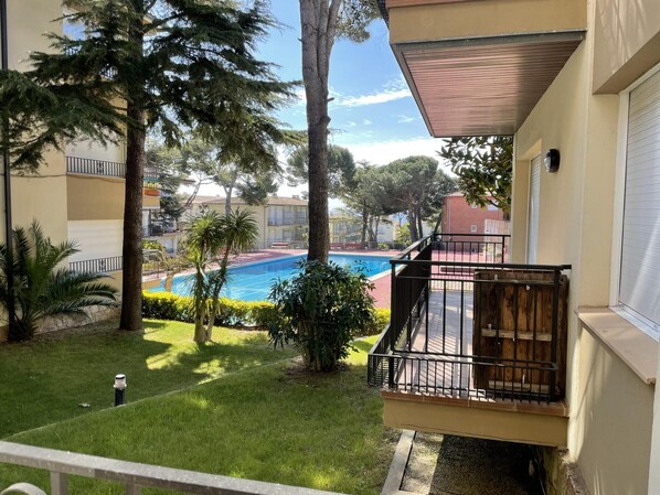 Un immeuble résidentiel doté d’un balcon donnant sur une piscine, le tout entouré d’arbres et de verdure.