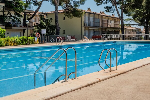 A swimming pool with metal railings, lounge chairs, and a building with balconies in the background.