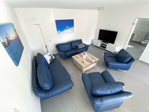 Una sala de estar moderna con sofás de cuero azul, una mesa de centro, un televisor de pantalla plana y un cuadro de un paisaje nevado.