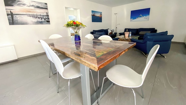 Un comedor moderno con una mesa de madera, sillas blancas y un jarrón de flores.