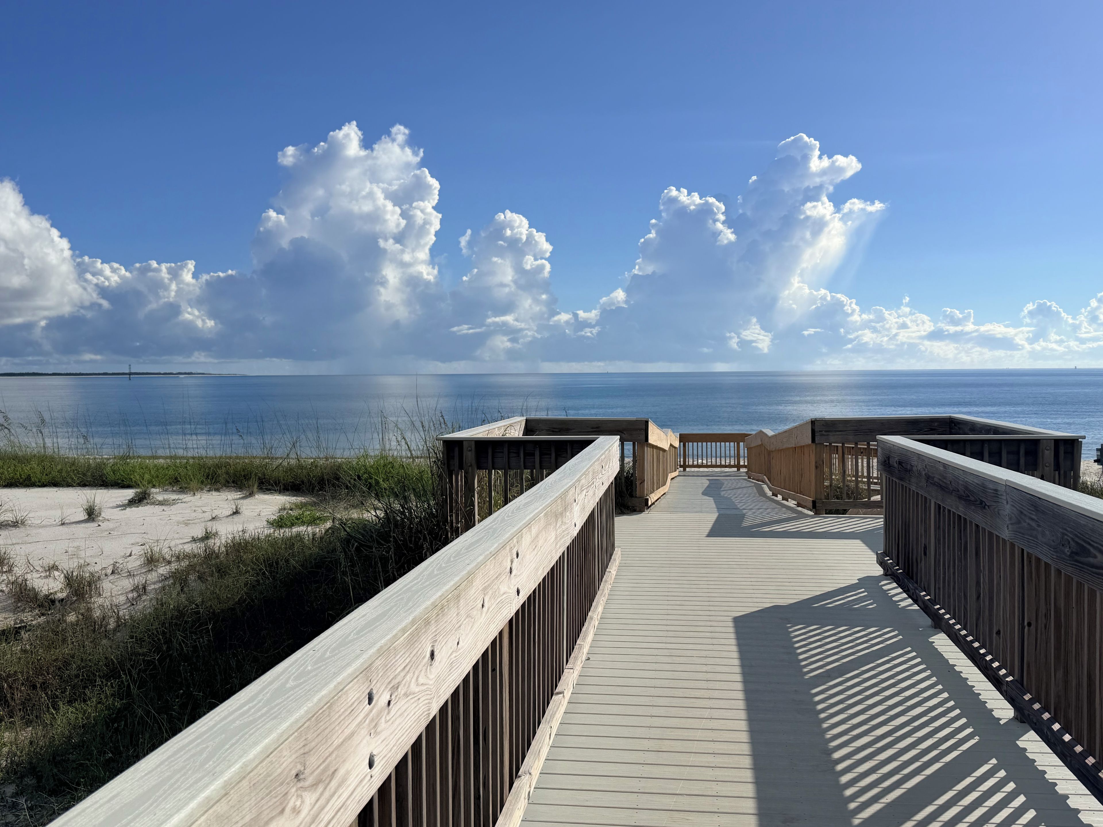 A wooden boardwalk leading to a beach with a clear view of the ocean and sky.