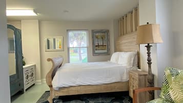 Un dormitorio con cama, una silla, una lámpara, un tocador y una ventana con persianas.
