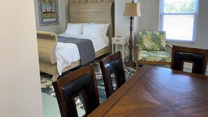 A bedroom with a bed, bedside table, lamp, chair, and a dining table.