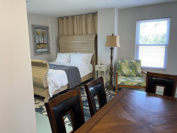 A bedroom with a bed, bedside table, lamp, chair, and a dining table. - Walk To The Beach At Beacon Hill. (Port St. Joe)