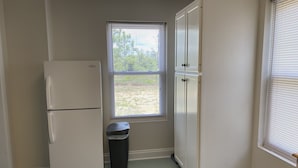 A compact kitchen with a white refrigerator, a trash bin, and a window with blinds.