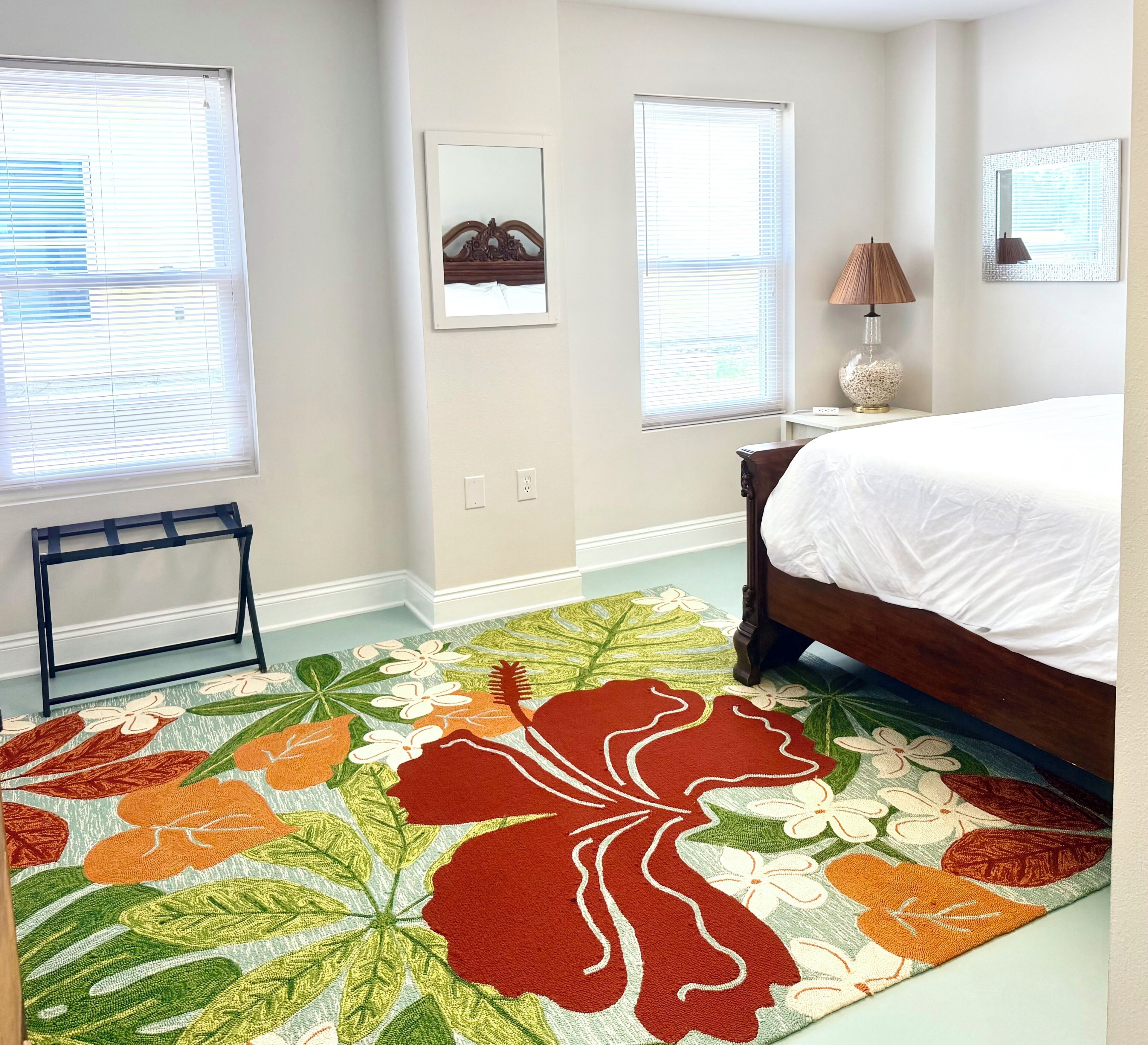 A bedroom with a bed, a standing lamp, and a floral area rug.