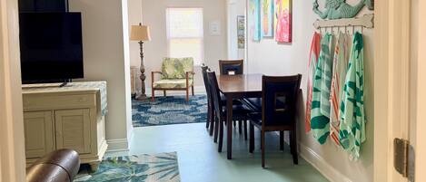 Un coin repas avec une table et des chaises, un téléviseur en arrière-plan et un mur décoré d’œuvres d’art.