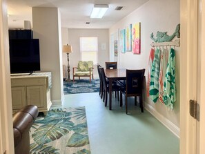 A dining area with a table and chairs, a television in the background, and a wall with artwork. - Walk To The Beach At Beacon Hill. (Port St. Joe)