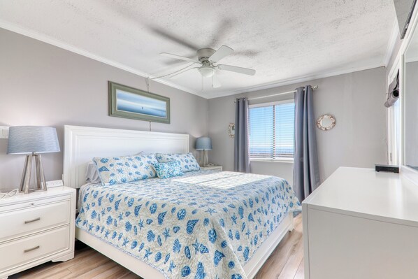 A bedroom with a bed, nightstands, a ceiling fan, a window with curtains, and a wall-mounted mirror.