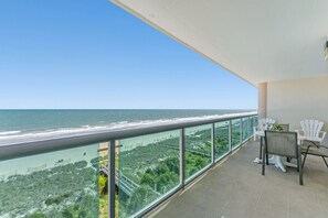 Un balcon avec vue sur l’océan, des chaises blanches et une table.