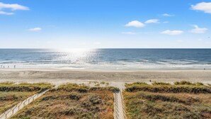 Une plage avec un ciel dégagé, un rivage sablonneux et un sentier qui mène à l’eau.