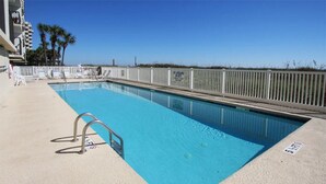 Une piscine avec un escalier en métal, entourée d’une clôture blanche, et un ciel bleu clair en arrière-plan.