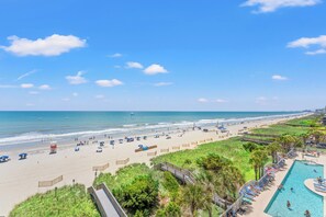 A beach resort with a swimming pool, beach umbrellas, and a lifeguard stand.