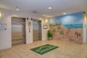 Un vestíbulo con dos ascensores, un mural de playa y una alfombra verde con el texto 'Crescent Shores'.