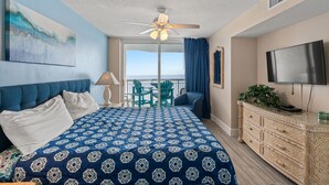 Una habitación de hotel con una cama grande, un ventilador de techo, televisión, balcón con vistas y un aparador de madera.