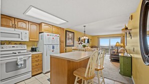 A kitchen with wooden cabinets, a white refrigerator, a microwave, and a stove. There is a bar area with two stools. - Nautical Watch 207-1BR/1BA Oceanfront condo in Windy Hill (North Myrtle Beach)