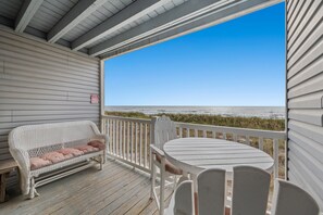 A wooden deck with a white bench and table, overlooking a beach.