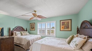 A bedroom with two beds, a ceiling fan, and a window with blinds. - Nautical Watch 207-1BR/1BA Oceanfront condo in Windy Hill (North Myrtle Beach)