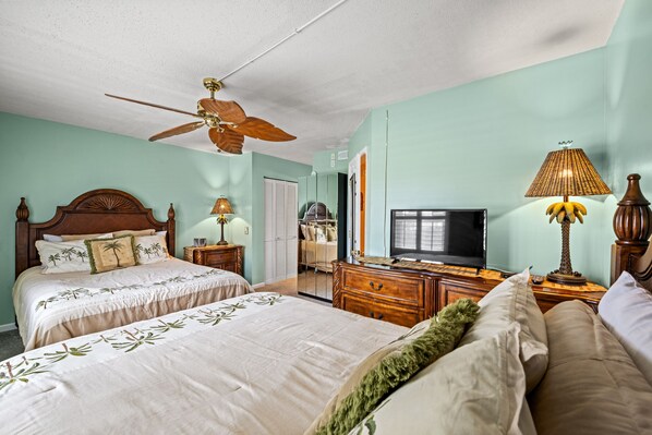 A bedroom with two beds, a ceiling fan, a television, and a dresser.