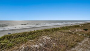 A coastal beach with a sandy path leading to the water, a lifeguard tower, and a clear sky.