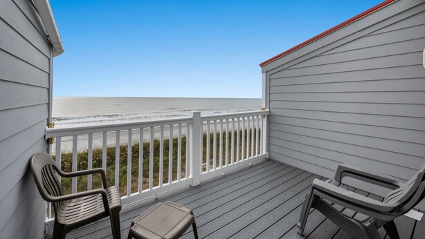 A covered deck with a view of the ocean, two chairs, and a small table.