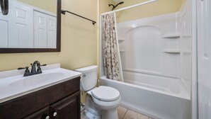 A bathroom with a white bathtub, a toilet, a sink with a mirror above it, and a shower curtain.