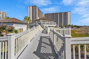 Stroll along the boardwalk to the beachfront property, offering access to a building above with modern architecture and balconies.