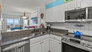 Una cocina con armarios blancos, un lavamanos de acero inoxidable, un microondas y una estufa.
