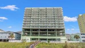 Un edificio a più piani con balconi, una scala che conduce all'ingresso e una zona sabbiosa davanti.