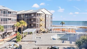 A multi-story hotel with a pool area, beach view, and outdoor seating.