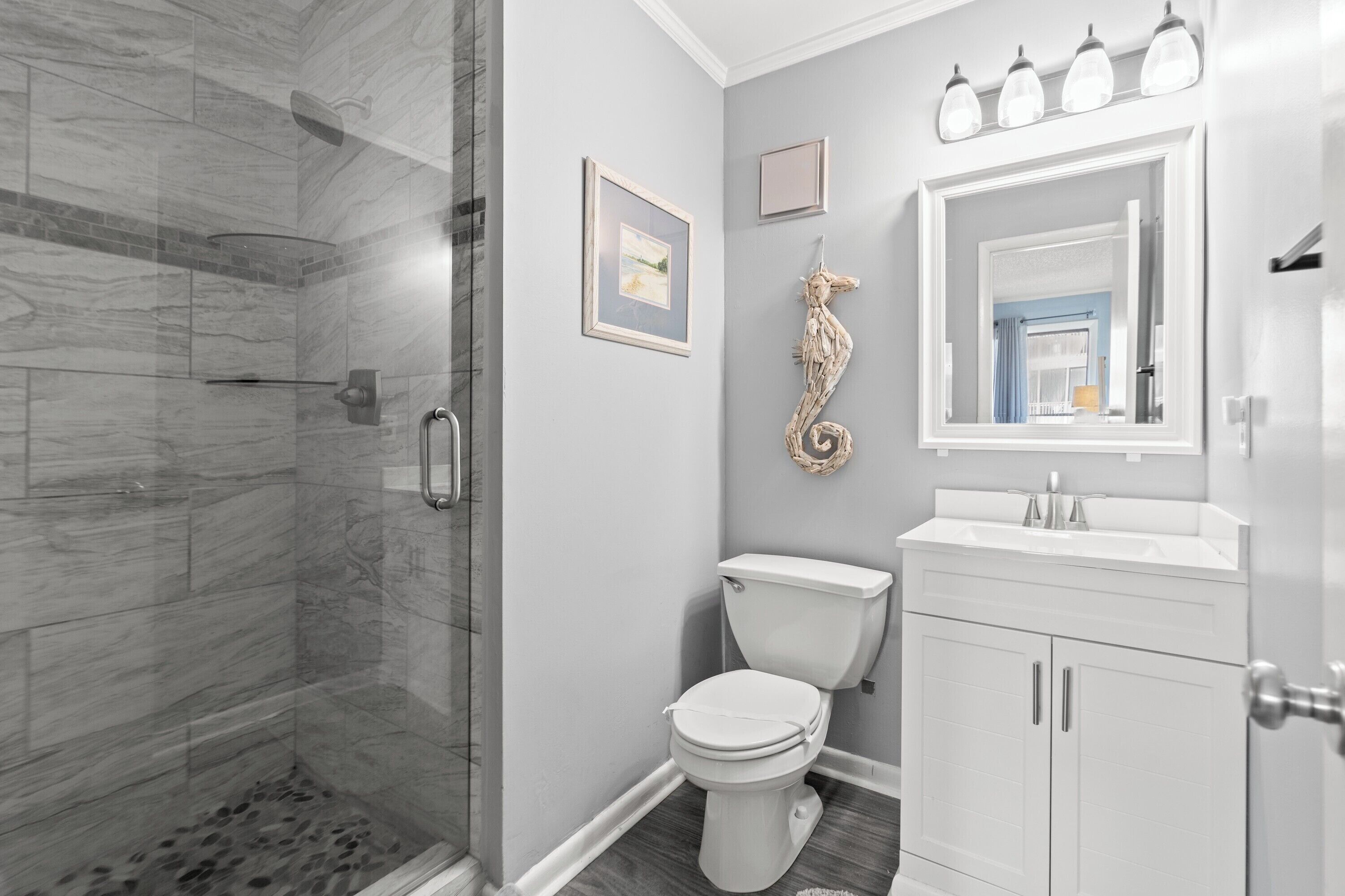 A bathroom with a glass-enclosed shower, a toilet, and a vanity with a mirror and lights.