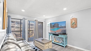 A modern living room with a leather sofa, a wooden coffee table, a teal entertainment unit, and a large TV on the wall.