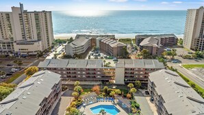 A hotel with multiple buildings, a swimming pool, and a beach view.