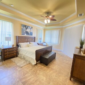 A bedroom with a large bed, a nightstand, a dresser, a bench, and a ceiling fan.