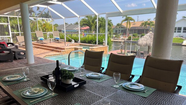 Une table à manger dressée pour quatre personnes, avec vue sur une piscine et des palmiers.