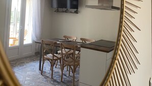 A dining area with a table and chairs, a television above the table, and a kitchen area with cabinets and a stove. - La Pépite des Tours (Châteaurenard)