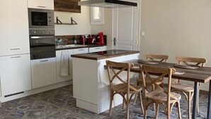 A modern kitchen with white cabinets, a built-in oven, and a microwave. There is a dining area with a wooden table and chairs. - La Pépite des Tours (Châteaurenard)