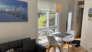 A modern living room with a grey sofa, a round table with two chairs, and a large window offering a view of snow-covered trees. - The MountainSide by Escapades Tremblant (Mont-Tremblant)