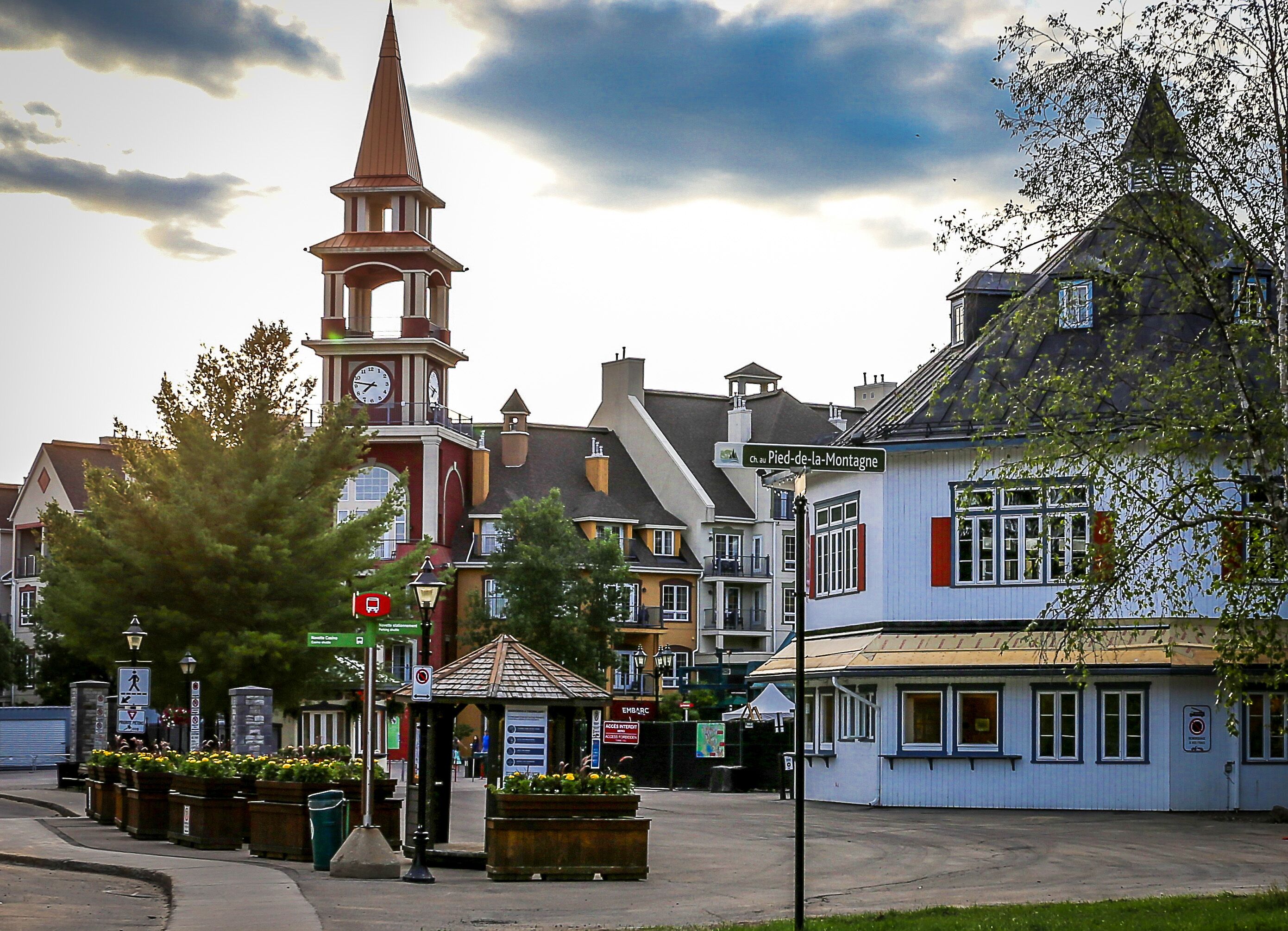 A town square with a prominent clock tower, a small kiosk, and various buildings with distinct architectural styles.